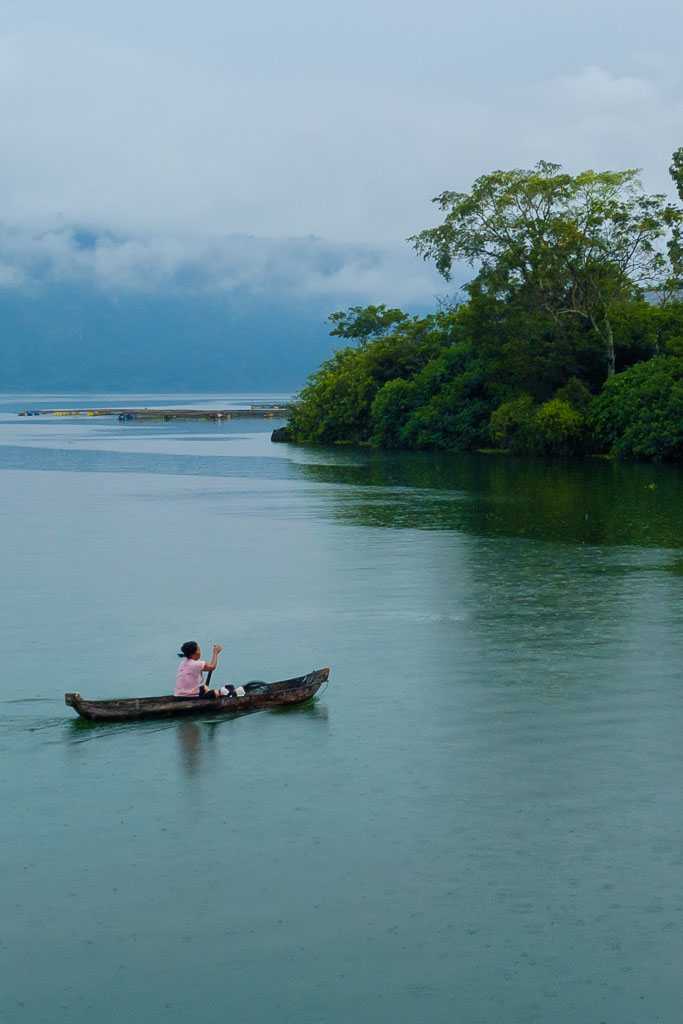 A balinese lady rowing in her boat while it is raining on the lake